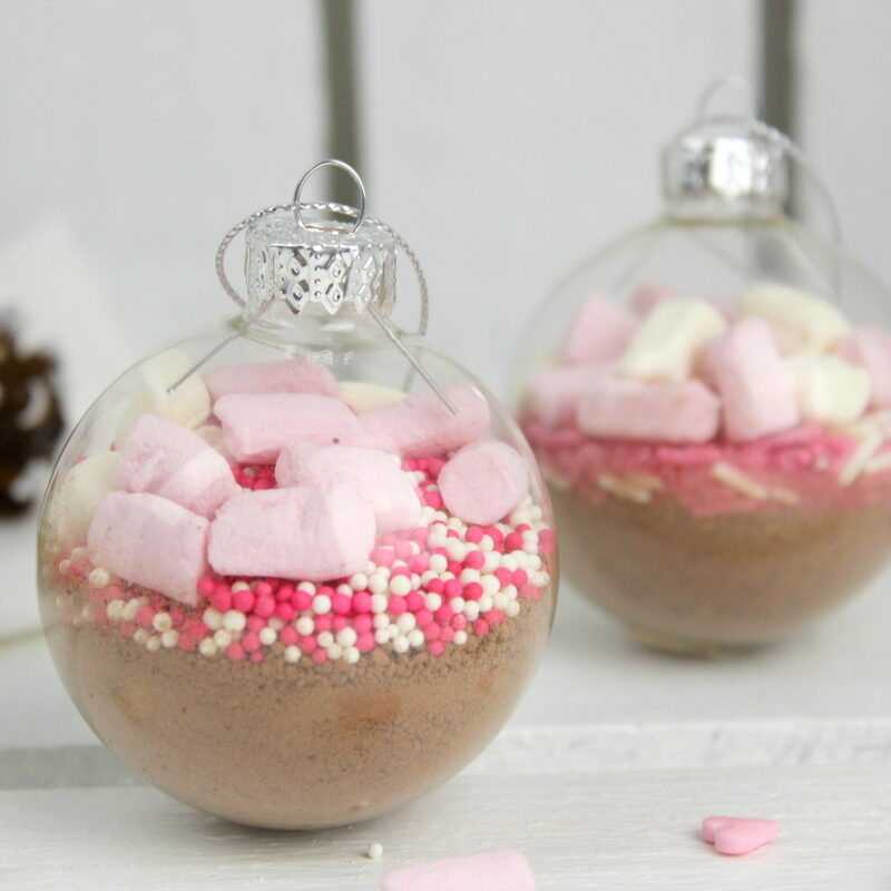 Trinkschokolade mit bunten Streuseln, Zuckerstange und Marshmallows in einer Christbaumkugel