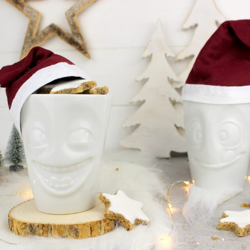 lustige Tassen mit Weihnachtsmannmützen gefüllt mit Zimtsternen
