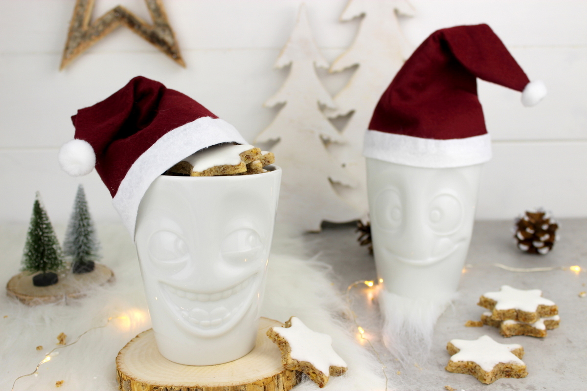 lustige Tassen mit Weihnachtsmannmützen gefüllt mit Zimtsternen